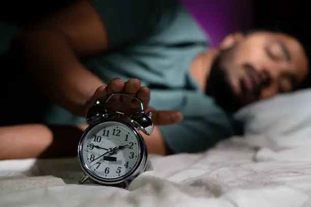 Photo of Focus on alarm, young man waking up early morning by turning off alarm - concept of active healthy lifestyle and morning routine.