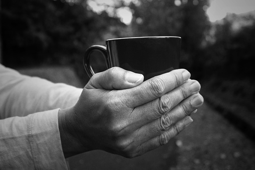 Person holding cup of coffee in hands on monochrome black and white abstract art background.