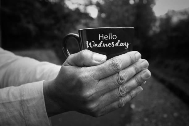 Person holding cup of morning tea or coffee in hands, with text - Hello Wednesday in black and white background. Person holding cup of morning tea or coffee in hands, with text - Hello Wednesday in monochrome black and white abstract art background. Happy Wednesday concept. wednesday morning stock pictures, royalty-free photos & images