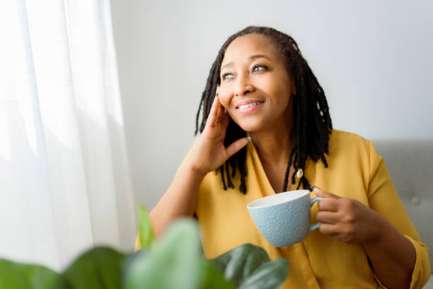 ritratto di una donna africana seduta sul divano con il caffè - gente serena foto e immagini stock