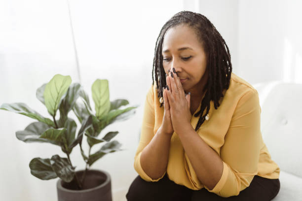 アフリカの女性の肖像画がソフに座って祈る - praying joy indoors lifestyles ストックフォトと画像