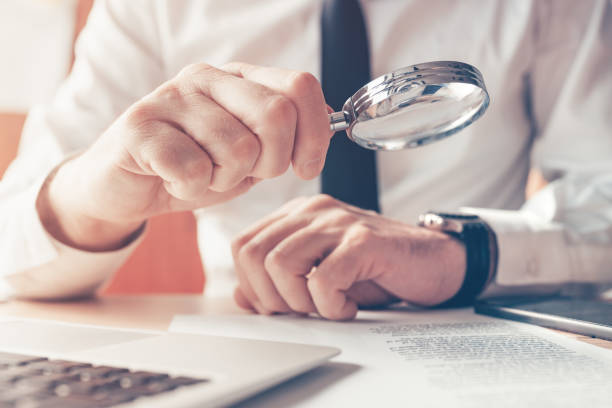 istock Cautious businessman reading contract agreement with magnifying glass 1369956435