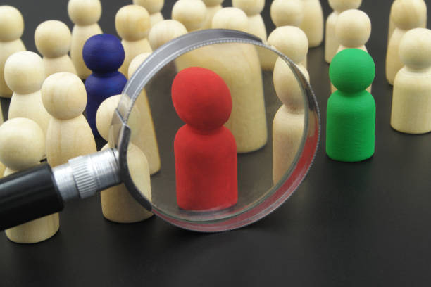 istock Colored people figures and common wooden people figures under magnifying glass on black background. 1369962280
