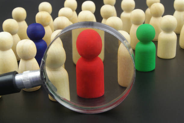 istock Colored people figures and common wooden people figures under magnifying glass on black background. 1369962294