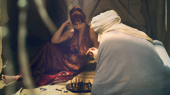 Chess gameplay on desert. Postapocalyptic mood, abandoned camp. Shamanic woman and man in Bedouin's outfit