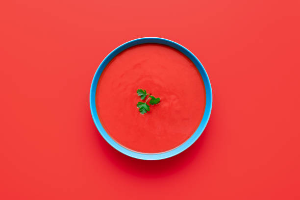 Tomato cream soup bowl, above view on a red background Above view with tomato cream soup in a blue bowl minimalist on a red table. Bowl of delicious soup isolated on a colored background. tomato soup stock pictures, royalty-free photos & images