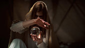 Mysterious female fortune teller holding glass sphere. Inside dark, desert tent