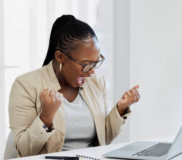 shot of a young businesswoman cheering while using a laptop in an office - excitement business person ecstatic passion imagens e fotografias de stock