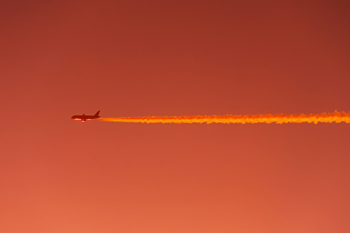 Airplane flies leaving contrail trace on a clear high in the red orange sky at sunset, air to air view