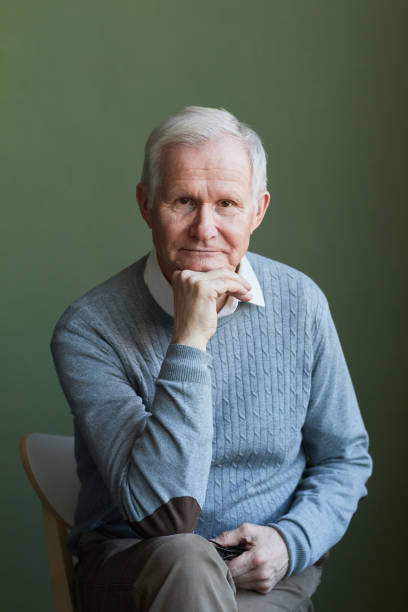 istock Serious elderly man in light blue pullover sitting on chair 1369974660