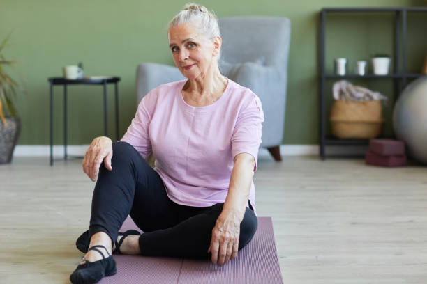 istock Happy active senior female looking at camera while sitting on mat 1369974665