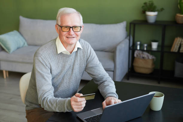 istock Smiling senior man with credit card looking at camera while shopping online 1369974682