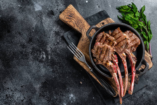 BBq Grilled lamb mutton chops steaks in a pan. Black background. Top view. Copy space