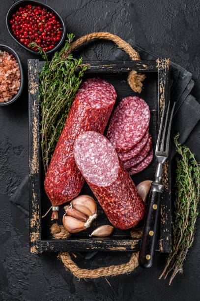 istock Sliced Dry salami sausage with fresh thyme. Black background. Top view 1369976115