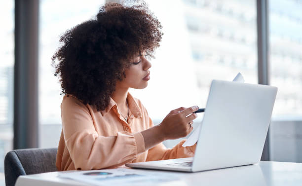 istock Shot of a young businesswoman reading documents while working on her laptop 1369976659