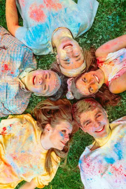 Photo of happy friends laying on green grass ground dirty in holi paints