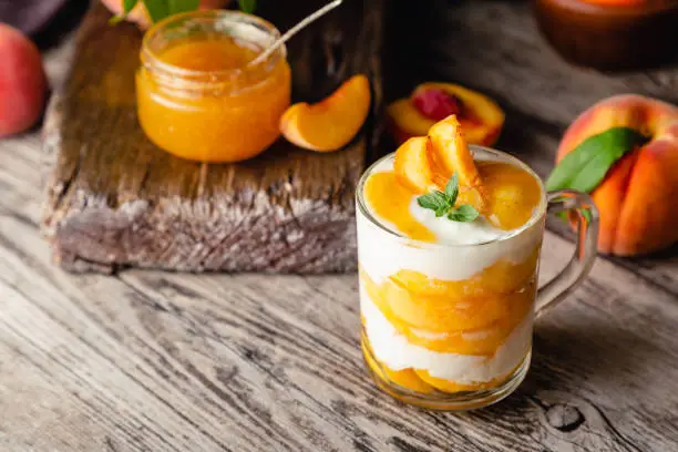 Peach fruit dessert in glass cup on wooden table. Homemade dessert with fruits. Fruit salad with yogurt or sour cream