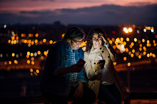 Senior man and young woman using mobile phone with city background bokeh effect