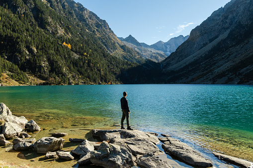 Young man traveler step on rocks on the shore of Lac de Gaube in French Pyrenees