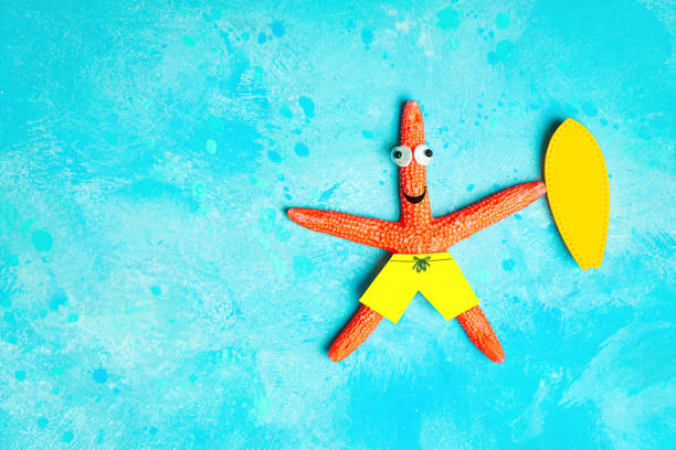 Funny starfish character with a yellow surfboard lying on a light blue background imitating water. Creative surfing vacation concept.