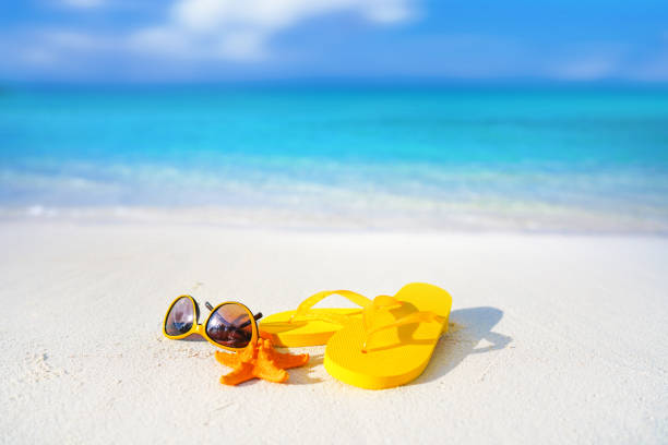 istock Beach accessories - sunglasses, starfish, yellow flip-flops on sandy tropical beach. 1369982379