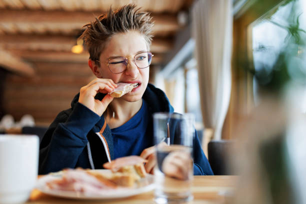 Teenage boy eating a very tough sandwich Little boy aged 12 eating breakfast. He is having hard time biting a sandwich made with hard, dry and stale bread. Canon R5 Teenager EatING stock pictures, royalty-free photos & images