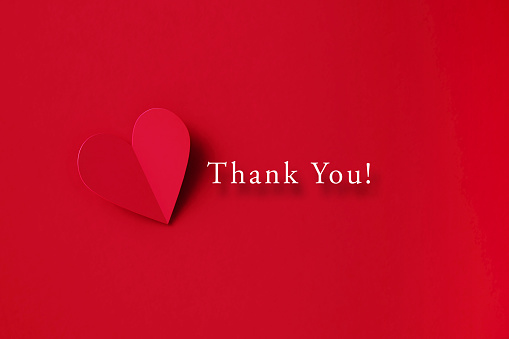 Thank You message next to a folding red heart shape on red background. Horizontal composition with copy space. Directly above. Thank you concept.