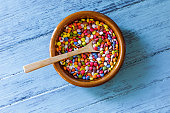 Table top view of small multicolored candies filled with chocolate inside clay dish with wooden spoon on blue wooden table. Analogy with a dish of legumes (lentils). Healthy food versus unhealthy food.