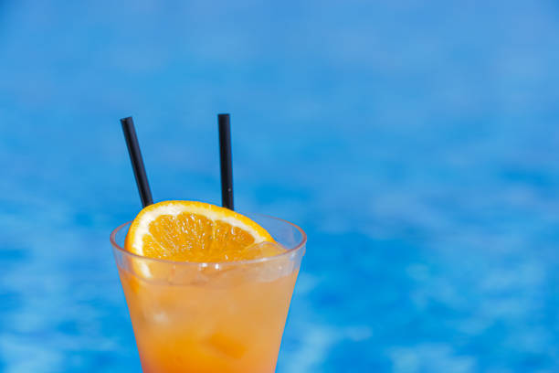 istock Orange cocktail with two straws on a blue pool background 1369991388