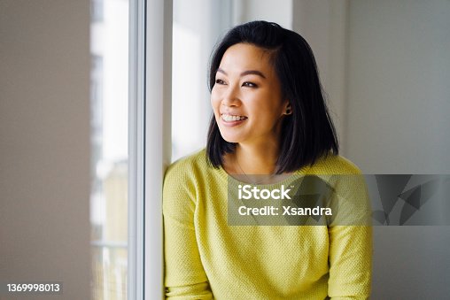 istock Smiling woman standing by the window at home 1369998013