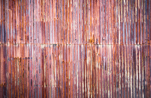 A large outdoor area of heavily corroded corrugated iron sheet with the rust weakening the metal surface.