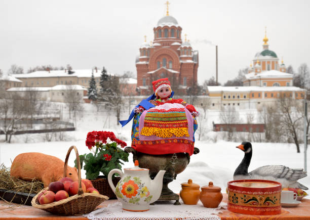 Table with samovar and teapot with decorations for celebration of Maslenitsa against backdrop of Pokrovsky Khotkov Monastery, Khotkovo, Russia