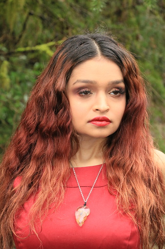 A model looking away and concentrating on something. She is wearing a red sleeveless dress and a necklace.