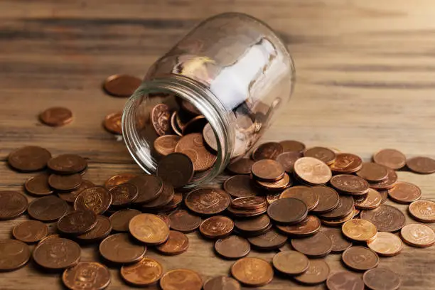 Photo of Shiny copper low value euro coins spilled from a glass jar.