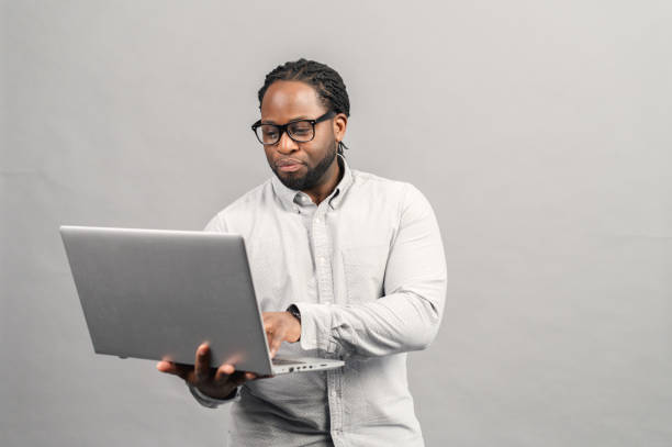 istock Smart African-American man using a laptop, isolated on grey 1370005504