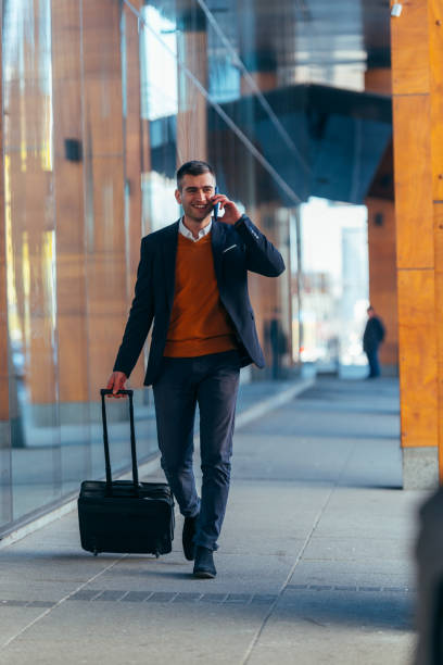 istock Young businessman walking through a station while talking on the phone and pulling his travel bag. 1370008262