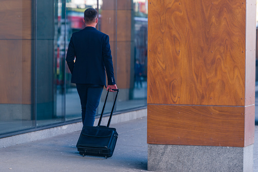 Close up photo a formal businessman dragging his suitcase, man bag, pull bag through a airport (station)