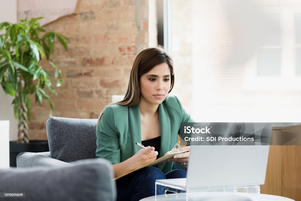 Mental health professional uses laptop to see clients Working from home, the young adult female mental health professional uses a laptop for teleconferencing with clients. Mental Health Professional Stock Photo