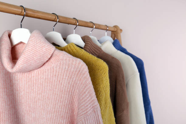 istock Warm sweaters hanging on wooden rack against light background, closeup 1370015517