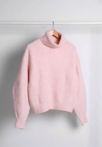 Warm sweater hanging on rack against white background