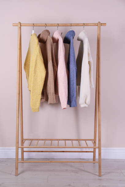 istock Warm sweaters hanging on wooden rack near pink wall 1370015913