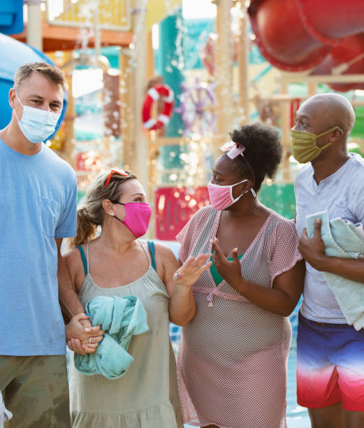 istock Two multiracial couples have fun at water park, in masks 1370016181