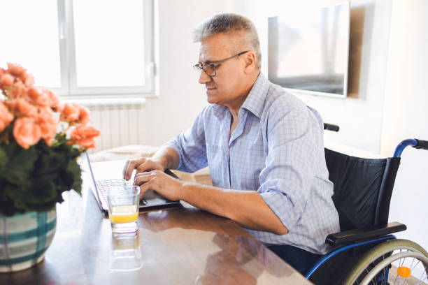 istock Disabled senior man in a wheelchair using a laptop 1370019628