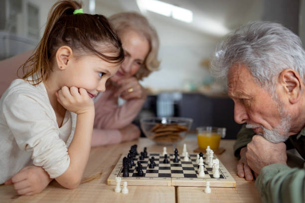 Close up of grandparents teaching a granddaughter how to play chess Close up of a Caucasian grandfather and grandmother teaching their little granddaughter how to play chess at home, bonding and having fun together senior chess stock pictures, royalty-free photos & images