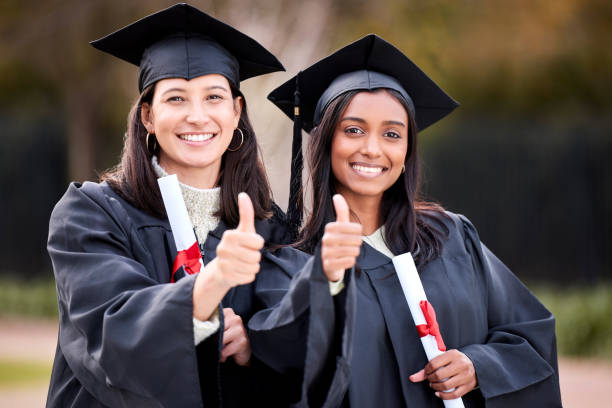 Portrait of two young women showing thumbs up on graduation day We did it! graduation photos stock pictures, royalty-free photos & images
