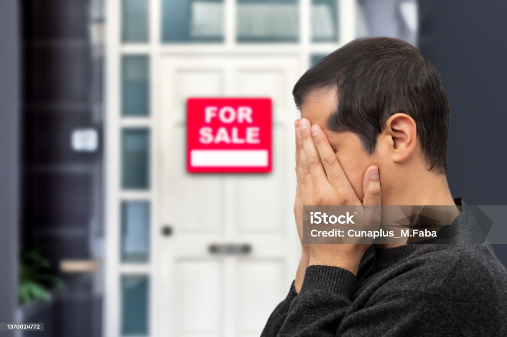 depressed man losing his house due to debts and mortgage Man extremely depressed and sad about losing his house key and seeing a for sale sign, real estate concept House Stock Photo