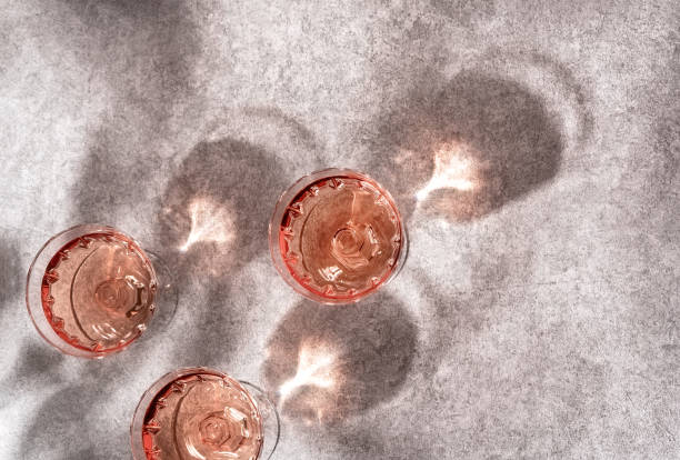 Top view of three crystal glasses of rose sparkling wine or champagne on grey stone background in hard light with shadows. Top view of three crystal glasses of rose sparkling wine or champagne on grey stone background in hard light with shadows. Minimal creative composition with copy space. Summer drink concept. champagne-glass-shadow stock pictures, royalty-free photos & images
