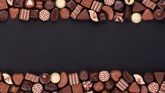 assorted candy of white and dark chocolate on black table background with empty space
