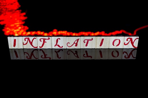 Concept of inflation heating up and spreading through the entire economy. The word inflation illuminated on a black background and reflected with simulated fire spreading across the word. Concept with copy space depicting inflation over heating and spreading.