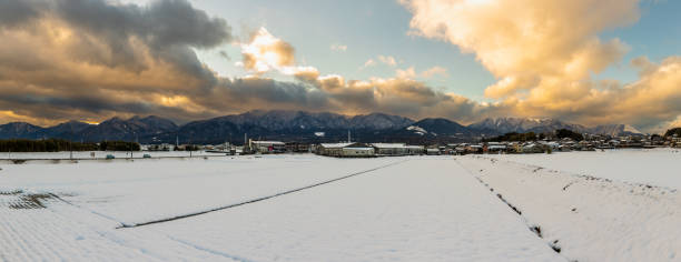 Snow covered rice farm fields with mountainous sunset background in the country side of rural Japan.